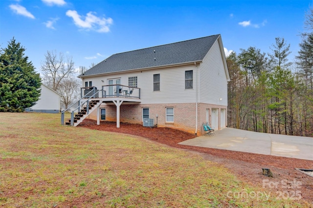 rear view of property with a deck, brick siding, stairs, driveway, and a lawn