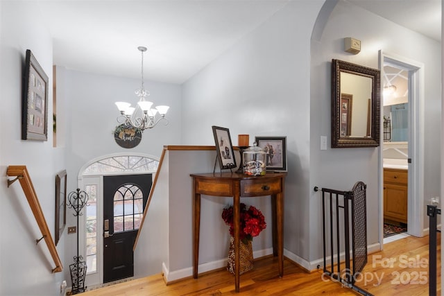 entrance foyer featuring light wood finished floors, stairs, arched walkways, and a notable chandelier