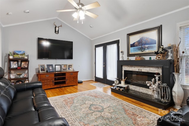 living room featuring a ceiling fan, lofted ceiling, ornamental molding, light wood-type flooring, and a fireplace