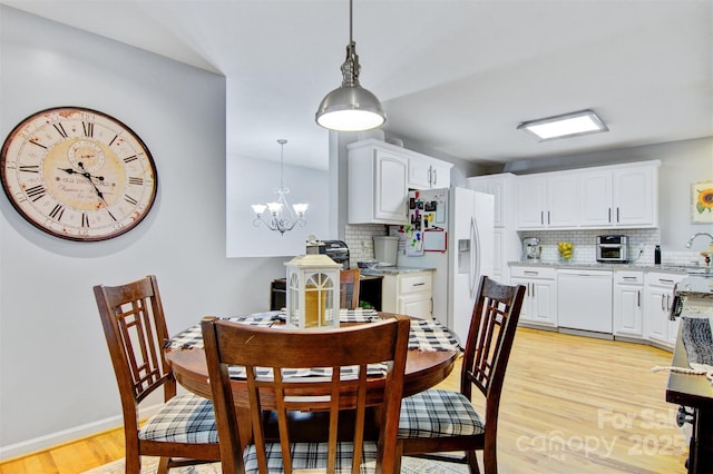 dining room with light wood finished floors, an inviting chandelier, and baseboards