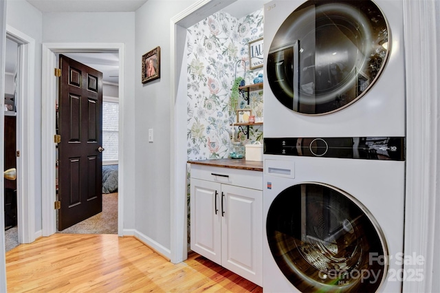 laundry area with light wood-type flooring, stacked washer / drying machine, cabinet space, and baseboards