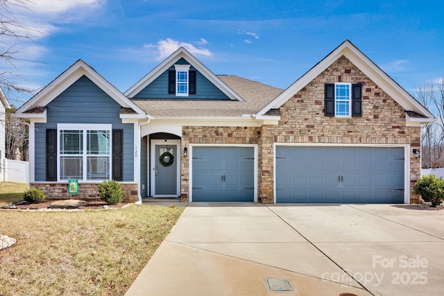 craftsman inspired home with a shingled roof, concrete driveway, a front yard, a garage, and stone siding