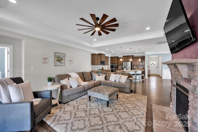 living area featuring recessed lighting, a raised ceiling, crown molding, and a stone fireplace