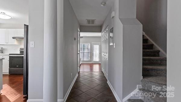 hall featuring dark tile patterned flooring, visible vents, baseboards, and stairs