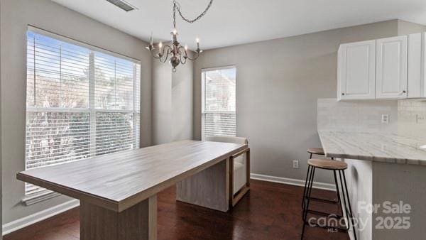 kitchen with white cabinetry, hanging light fixtures, visible vents, and a kitchen bar