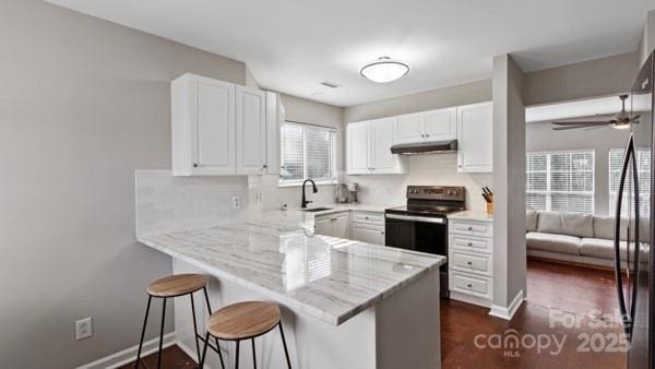 kitchen with a peninsula, under cabinet range hood, white cabinetry, and a kitchen breakfast bar