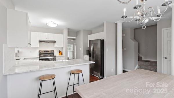 kitchen featuring white cabinets, a peninsula, light stone countertops, stainless steel appliances, and under cabinet range hood