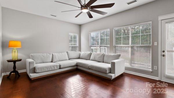 living area featuring ceiling fan, visible vents, dark wood finished floors, and baseboards