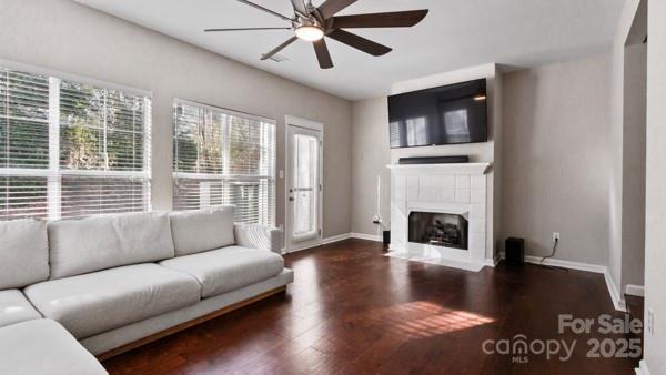 unfurnished living room featuring dark wood-style floors, ceiling fan, a tile fireplace, and baseboards