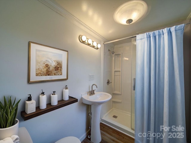 bathroom with a stall shower, toilet, crown molding, and a sink