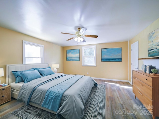 bedroom featuring light wood finished floors, multiple windows, baseboards, and a ceiling fan