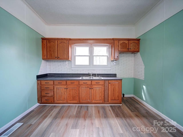 kitchen with dark countertops, light wood-style floors, visible vents, and a sink