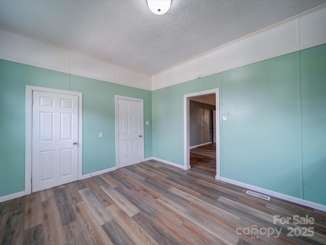 unfurnished room with visible vents, a textured ceiling, light wood-style flooring, and baseboards