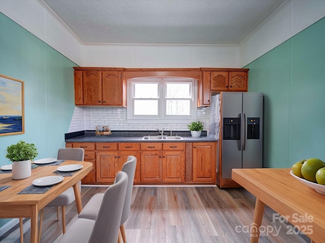 kitchen featuring brown cabinets, dark countertops, light wood-style floors, a sink, and stainless steel fridge with ice dispenser
