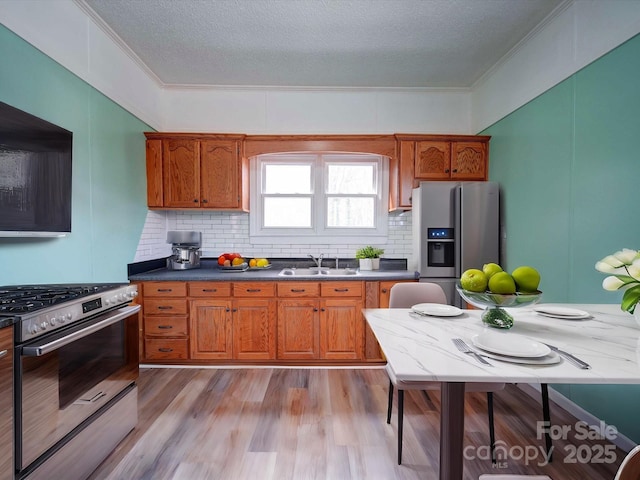 kitchen with stainless steel appliances, brown cabinets, a sink, and light wood finished floors