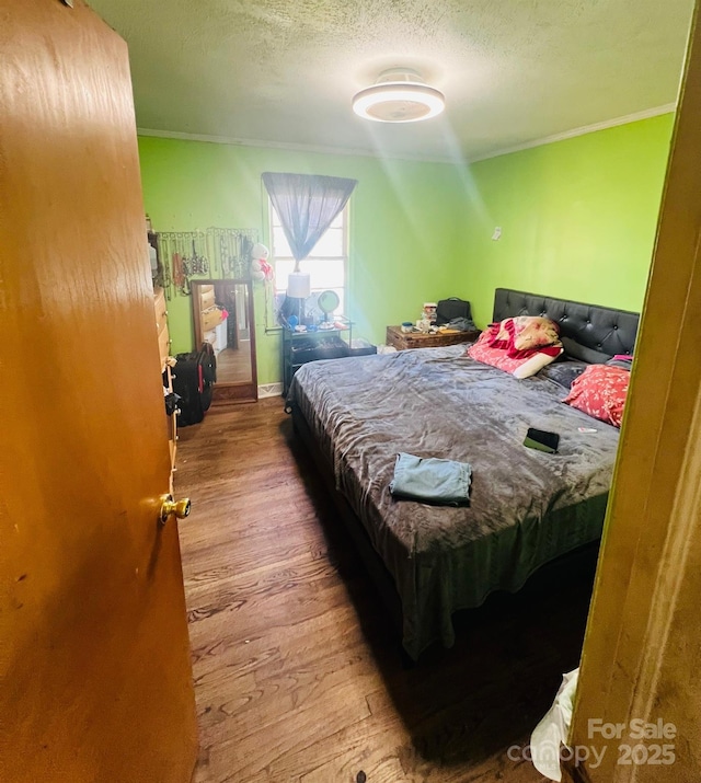 bedroom with a textured ceiling, ornamental molding, and wood finished floors