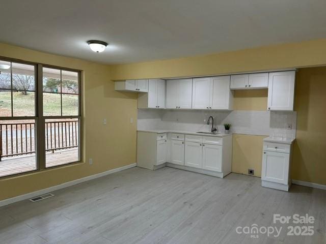 kitchen featuring light countertops, visible vents, white cabinets, a sink, and light wood-type flooring