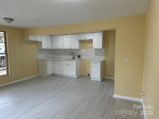 kitchen with light countertops, light wood-style flooring, white cabinetry, a sink, and baseboards