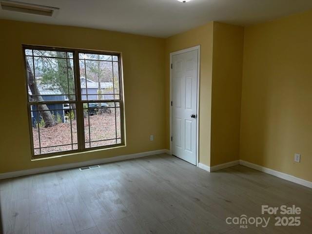 unfurnished room with light wood-type flooring, visible vents, and baseboards