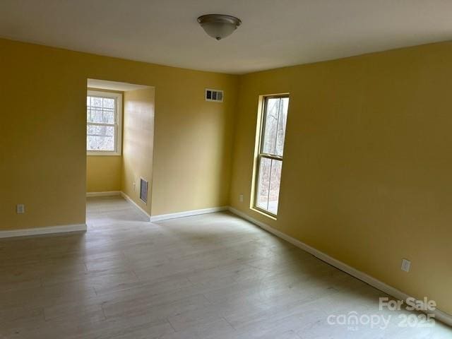 empty room with a healthy amount of sunlight, light wood finished floors, baseboards, and visible vents