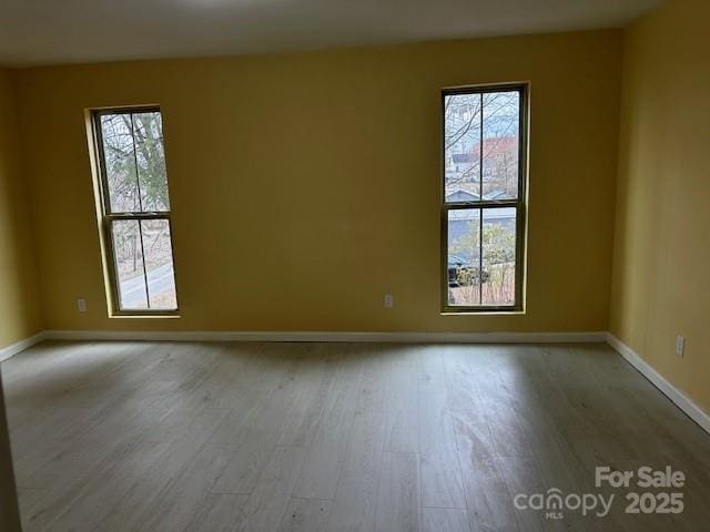 empty room featuring light wood-type flooring, plenty of natural light, and baseboards