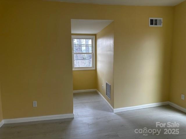 unfurnished room featuring light wood-type flooring, visible vents, and baseboards