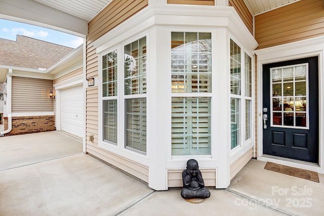 entrance to property featuring an attached garage, a porch, concrete driveway, and roof with shingles