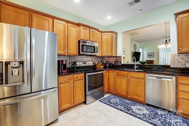 kitchen with a sink, visible vents, appliances with stainless steel finishes, brown cabinets, and dark stone countertops