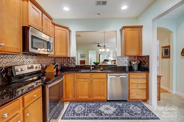 kitchen featuring visible vents, dark stone counters, appliances with stainless steel finishes, brown cabinets, and a sink