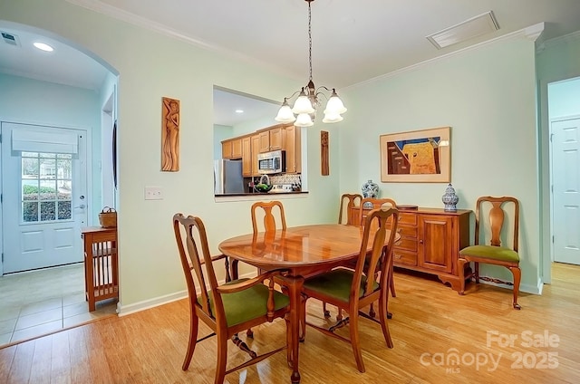 dining space with arched walkways, light wood finished floors, visible vents, and crown molding