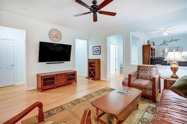 living area featuring light wood finished floors, ceiling fan, baseboards, and crown molding