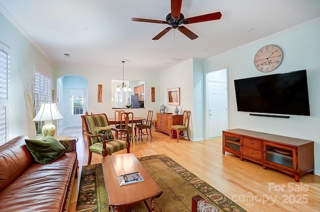 living area featuring light wood-style flooring, arched walkways, crown molding, and ceiling fan with notable chandelier