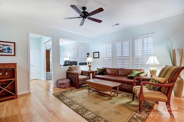 living room with crown molding, visible vents, a ceiling fan, and light wood-style floors