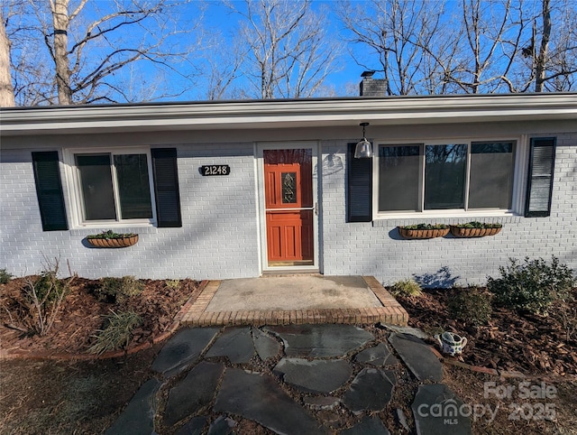 doorway to property with brick siding and a chimney