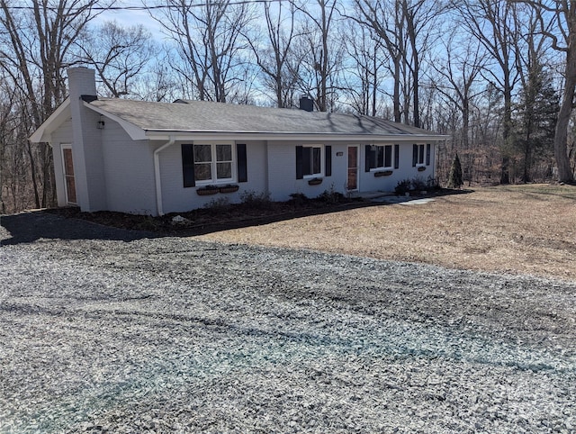 view of front facade with gravel driveway, brick siding, a chimney, and roof with shingles