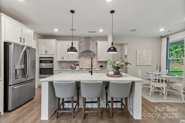 kitchen with white cabinetry, hanging light fixtures, appliances with stainless steel finishes, light countertops, and wall chimney exhaust hood