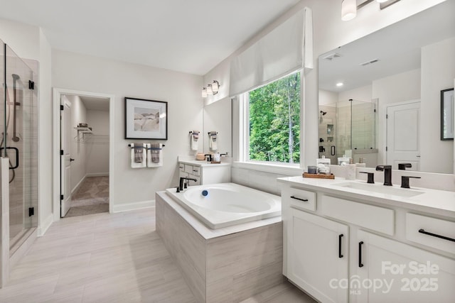 bathroom featuring a sink, a garden tub, a spacious closet, a shower stall, and two vanities