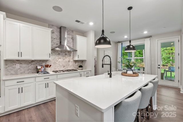 kitchen featuring a sink, visible vents, wall chimney exhaust hood, wood finished floors, and a center island with sink