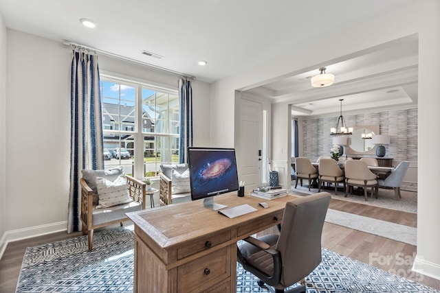 home office featuring a notable chandelier, a raised ceiling, visible vents, baseboards, and wood finished floors