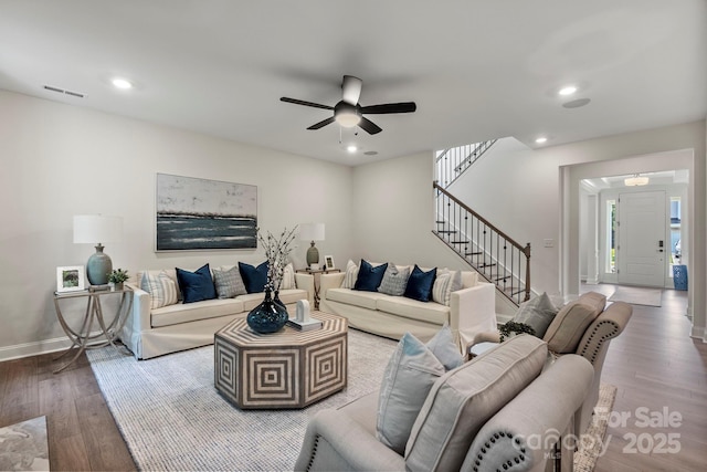 living room featuring visible vents, baseboards, wood finished floors, a ceiling fan, and stairs
