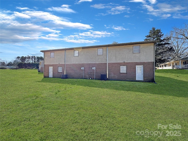 back of property with central air condition unit, brick siding, and a yard