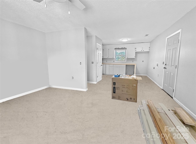 unfurnished living room with light carpet, ceiling fan, a textured ceiling, and baseboards