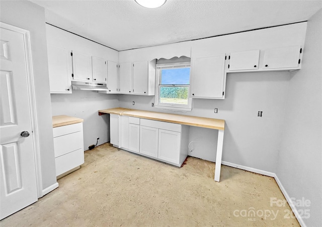 kitchen featuring a textured ceiling, under cabinet range hood, baseboards, white cabinets, and built in study area