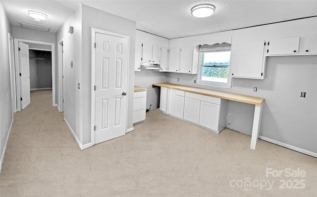 kitchen with a textured ceiling, under cabinet range hood, baseboards, white cabinets, and built in study area