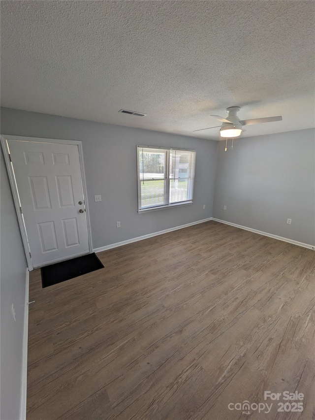 unfurnished room with ceiling fan, dark wood-type flooring, visible vents, and baseboards