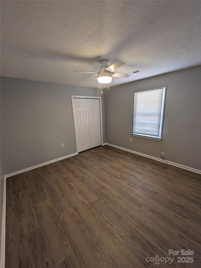 unfurnished bedroom featuring ceiling fan, dark wood-type flooring, visible vents, baseboards, and a closet