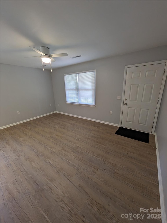 empty room featuring dark wood-style flooring, visible vents, and baseboards