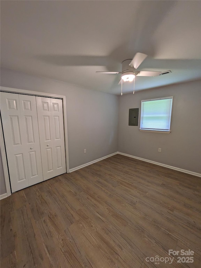 unfurnished bedroom featuring dark wood finished floors, a closet, visible vents, electric panel, and baseboards