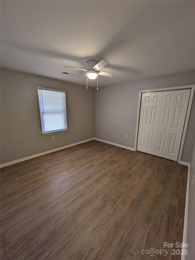 unfurnished bedroom featuring visible vents, baseboards, a ceiling fan, dark wood-style floors, and a closet