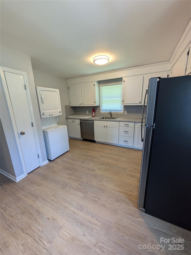 kitchen with stacked washer and dryer, appliances with stainless steel finishes, a sink, and white cabinets